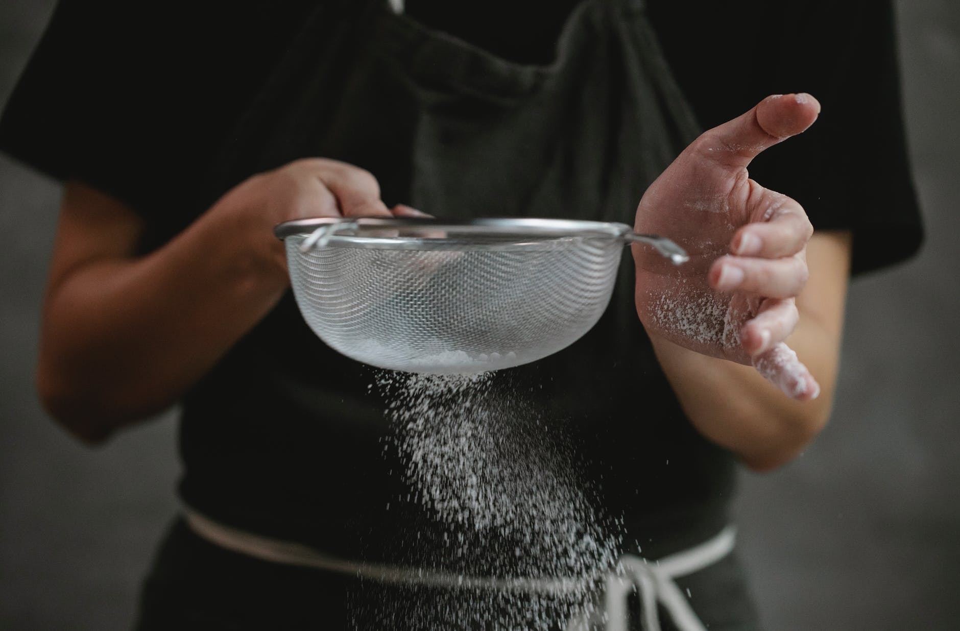 person pouring flour from sieve in kitchen